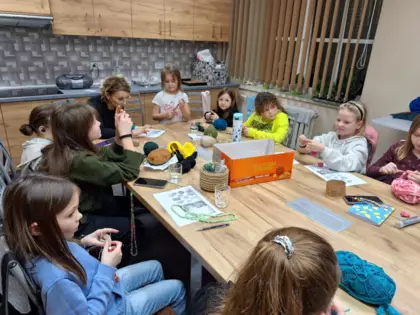 Uczestniczki warsztatów szydełkowania siedzą przy stole i szydełkują