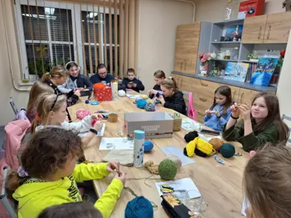 Uczestniczki warsztatów szydełkowania siedzą przy stole i szydełkują