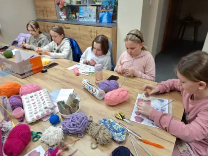 Uczestniczki warsztatów szydełkowania siedzą przy stole i szydełkują