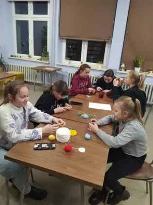 Uczestniczki zajęć siedzą przy stole i szydełkują.