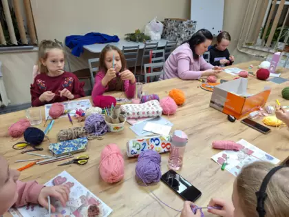 Uczestniczki warsztatów szydełkowania siedzą przy stole i szydełkują.