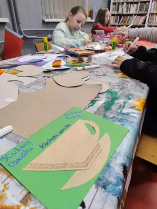 Dziewczynki siedzą przy stole i wykonują laurkę dla dziadka.