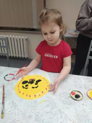 Dziewczynka maluje żółta farbą twarz kubusia.