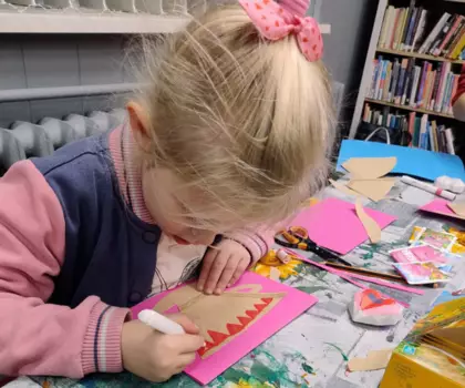 Dziewczynka mazakiem maluje laurkę dla babci.