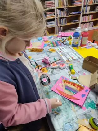 Dziewczynka mazakiem maluje laurkę dla babci.