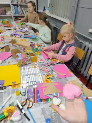 Dziewczynki wycinają z kolorowego papieru laurkę dla babci i dziadka.