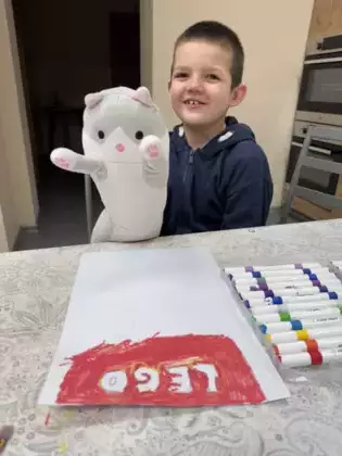 Chłopczyk trzyma w ręku kota a przed nim na stole leży list.