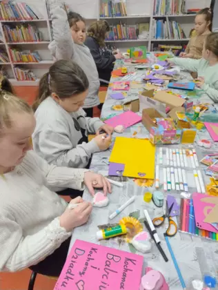 Dzieci siedzą przy stoliku i wykonują laurki dla babci i dziadka.