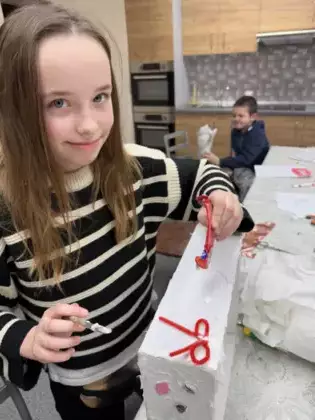 Dziewczynka przykleja kokardki do kartona, w tle widać chłopczyka z kotkiem.