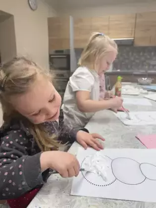 Dziewczynki pianką wyklejają bałwanka.