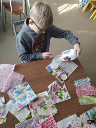 Chłopak okleja słoik kolorowymi serwetkami.