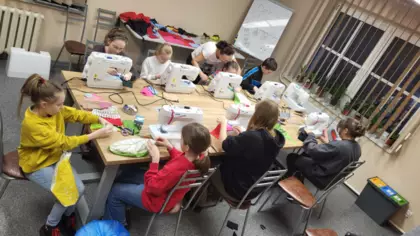 Uczestnicy zajęć siedzą przy maszynach na zajęciach krawieckich i szyją poduszki.