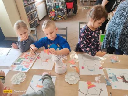 Przedszkolaki ubierają bałwanki wyciętymi elementami ubrania.