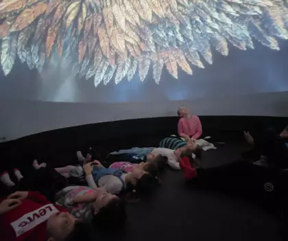 Uczestnicy leżą na podłodze w kopule kina sensorycznego i oglądają seans filmowy