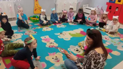 Dzieci w przedszkolu słuchają bajki o kotku czytanej przez panią bibliotekarkę.