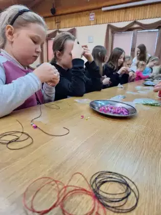 Uczestniczki warsztatów nawlekają koraliki na sznurek.