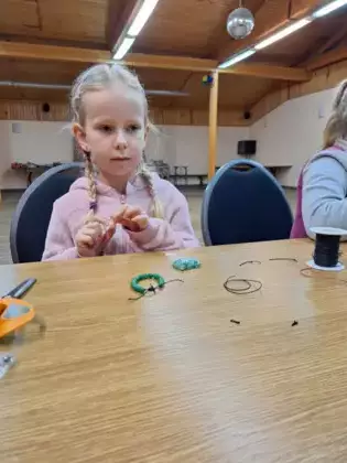 Dziewczynka związuje zrobioną bransoletkę.