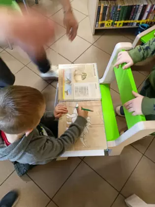 Przedszkolak koloruje książeczkę o dinozaurach.