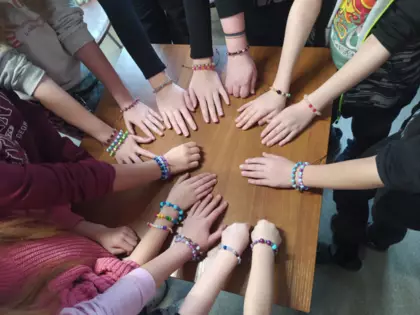 dzieci pokazują ręce na których są kolorowe bransoletki wykonane na zajęciach.