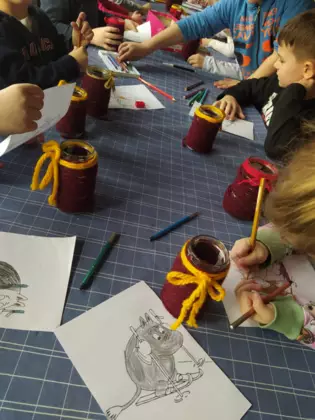 Dzieci siedzą przy stoliku i kolorują obrazki.