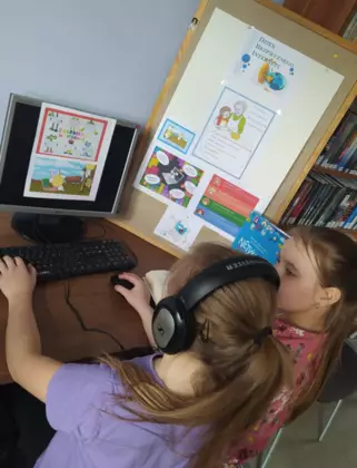 Dziewczynki korzystają z komputera w czytelni bibliotecznej.