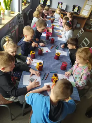 Dzieci siedzą przy stoliku i kolorują obrazki.