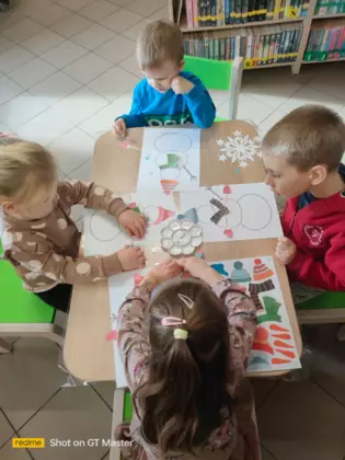 Przedszkolaki ubierają bałwanki wyciętymi elementami ubrania.