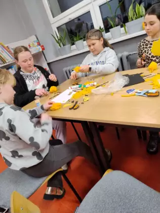 Uczestnicy przy stole wykonują pompony z wełny.