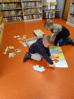 Dwóch chłopców układa duże puzzle z Kubusia Puchatka.