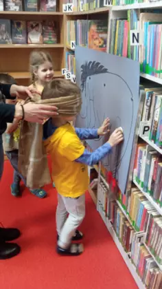 Chłopczyk z zawiązanymi oczami przykleja ogon osiołkowi.