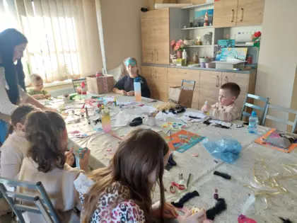 Uczestnicy zajęć siedzą przy stole i wykonują kolorowe maski karnawałowe