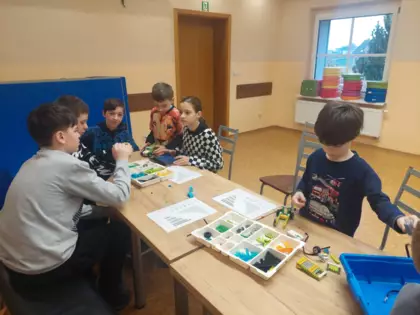 Chłopcy siedzą przy stole i składają autka z klocków Lego