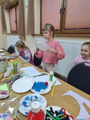 Dziewczynka wycina z papierowego talerzyka ozdobę.