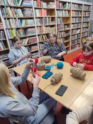 Uczestniczki warsztatów szydełkowania siedzą przy stole i wykonują pierwsze kroki.
