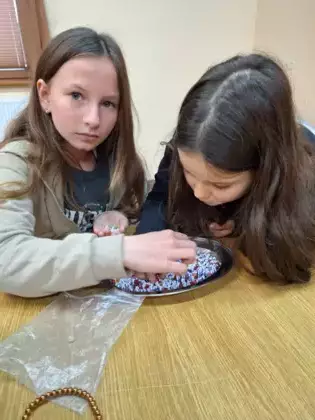 Dziewczyny nawlekają kolorowe koraliki na sznureczek.