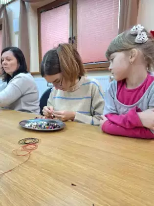 Instruktorka pokazuje uczestniczkom jak tworzyć kolorową biżuterię.