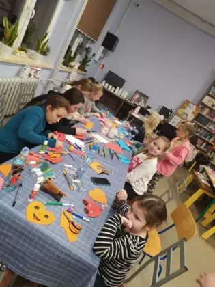 Dzieci siedzą przy stole i wykonują prace plastyczne.