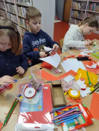 Dzieci siedzą przy stole i wyklejają serca z papieru.