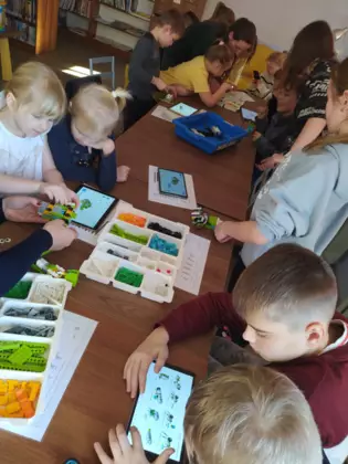 Uczestnicy warsztatów przy stole układają klocki Lego.