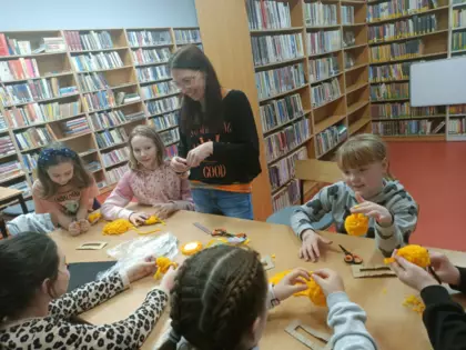 Uczestnicy przy wspólnym stole wykonują pompony z wełny.