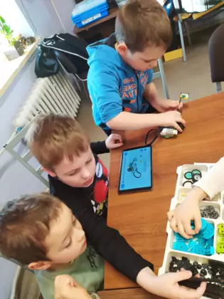 Uczestnicy warsztatów przy stole układają klocki Lego.