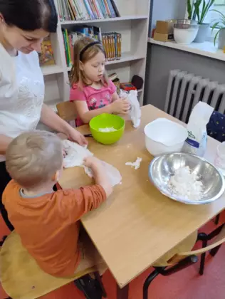 Dzieci siedzą przy stoliku i wykonują sztuczny śnieg.