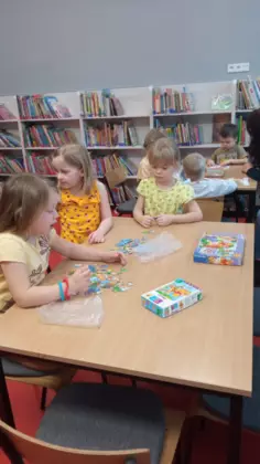 Dzieci siedzą przy stolikach i układają puzzle.