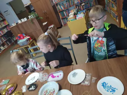 Chłopak i dziewczynki nawlekają koraliki na sznurek.