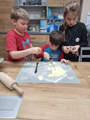 Chłopcy wycinają i składają z ciasta faworki.