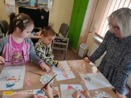Przedszkolaki ubierają bałwanki wyciętymi elementami ubrania.