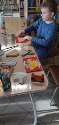 Chłopak siedzi przy stole i wykleja pracę dla babci.