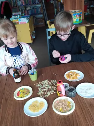 Uczestnicy zajęć oklejają słoik koralikami.