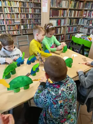 Przedszkolaki wykonują dinozaury z talerzyków papierowych.