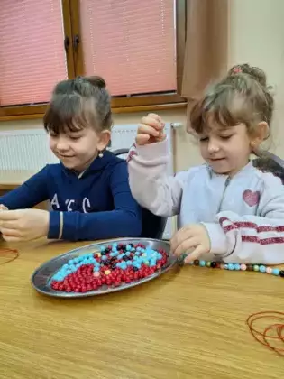 Dziewczynki nawlekają koraliki na kolorowy sznurek.